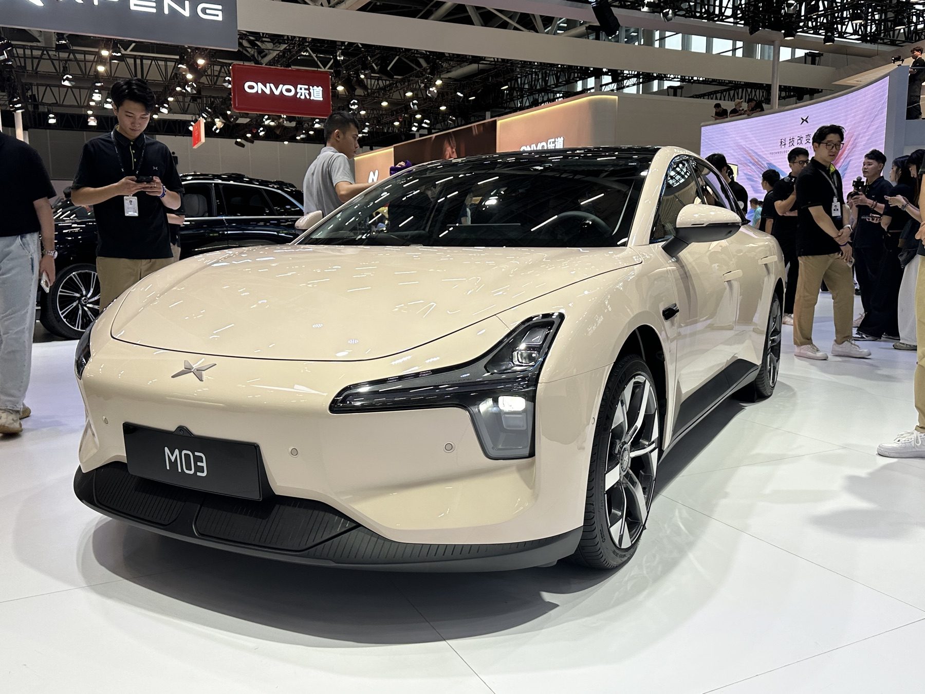 Cream XPeng MONA M03 on a motor-show stand, front three-quarter view